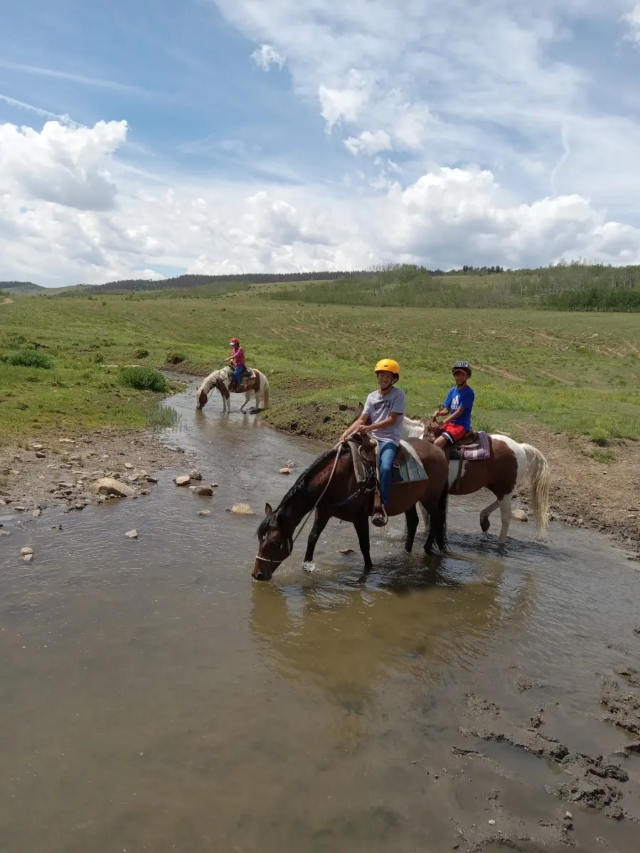 People horseback riding across a small stream.